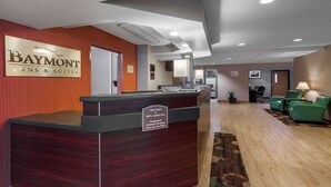 A reception desk with a sign indicating the hotel name and amenities, a waiting area with green chairs, and a carpeted floor.