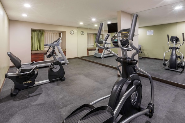 Un gimnasio con cintas de correr, elípticas y un espejo grande.