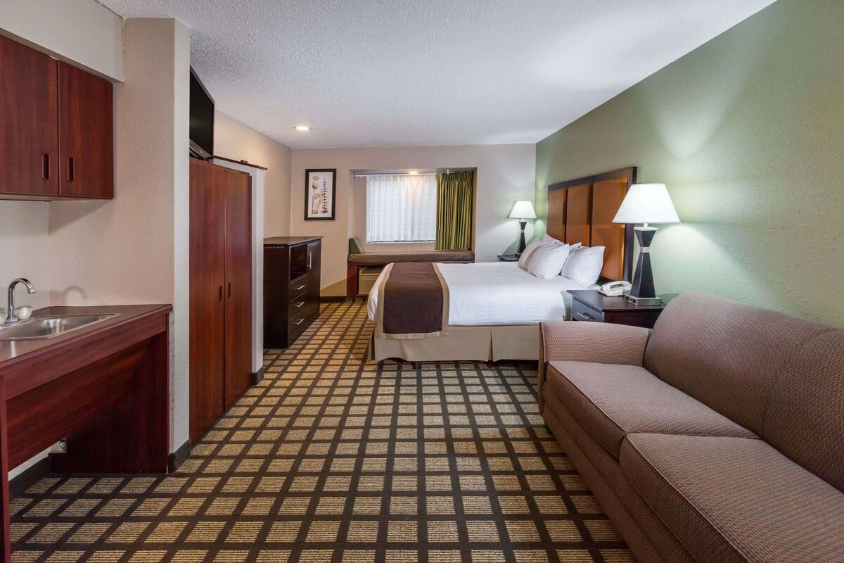 A hotel room with a bed, a sofa, a desk, a lamp, a window with curtains, and a checkered floor.