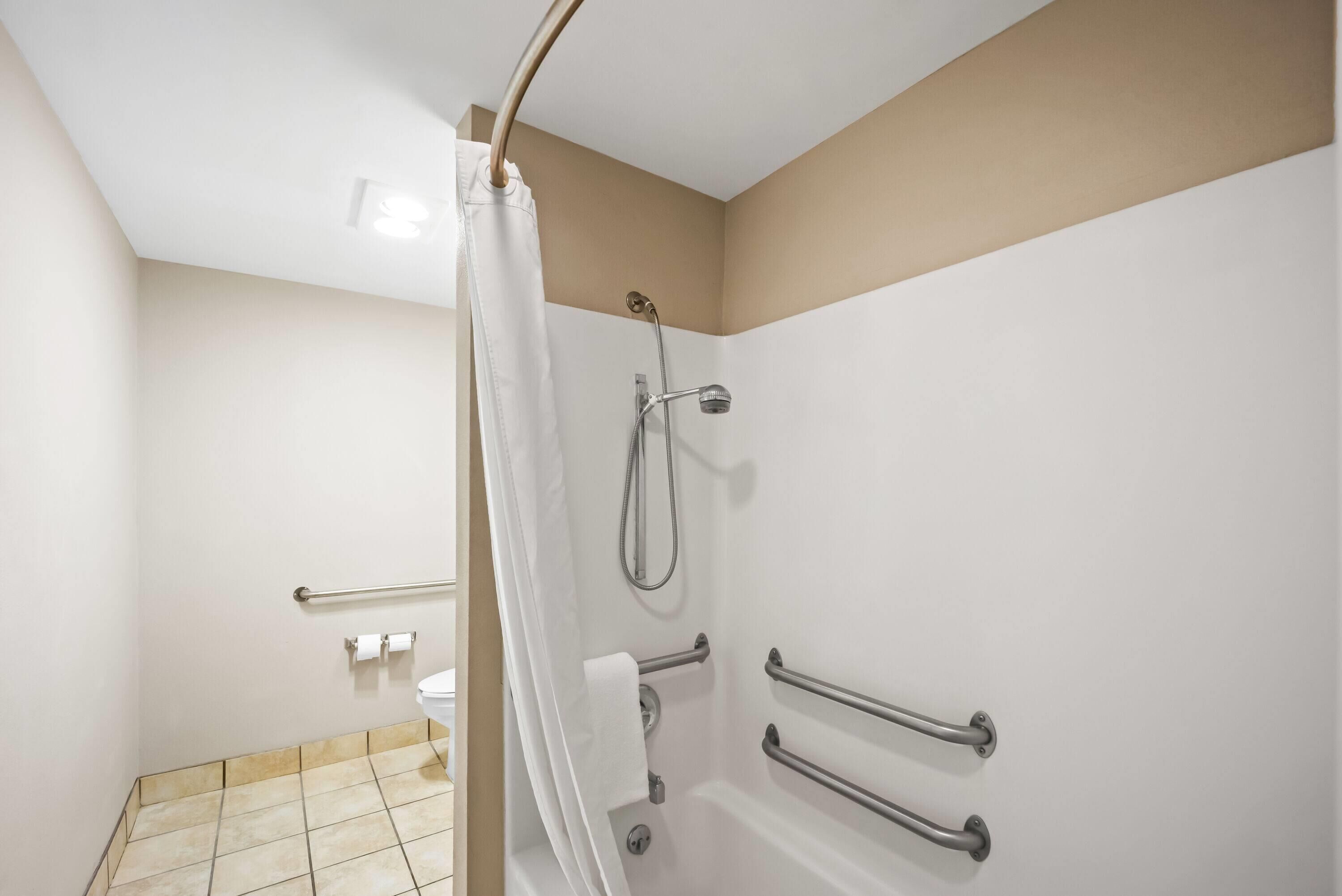 A bathroom with a shower, grab bars, and a toilet.