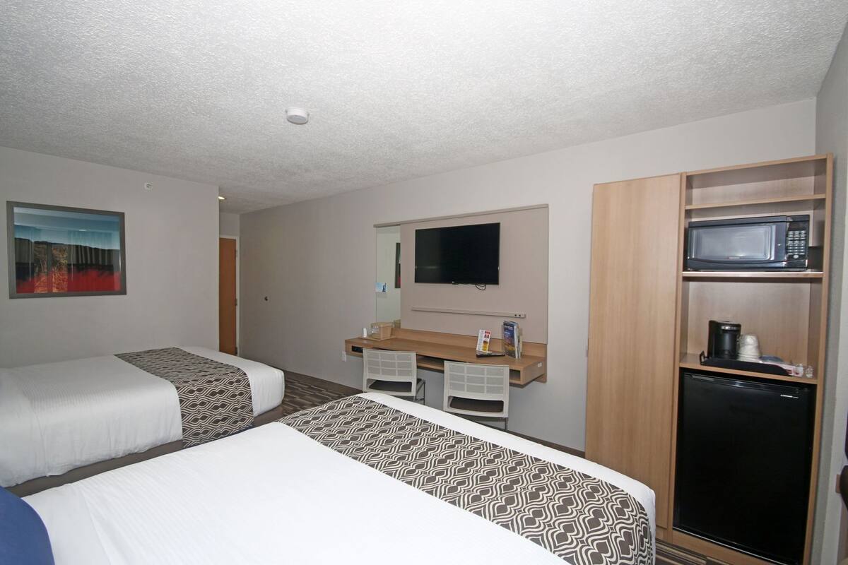 A hotel room with two beds, a desk with a chair, a television, a microwave, and a refrigerator.