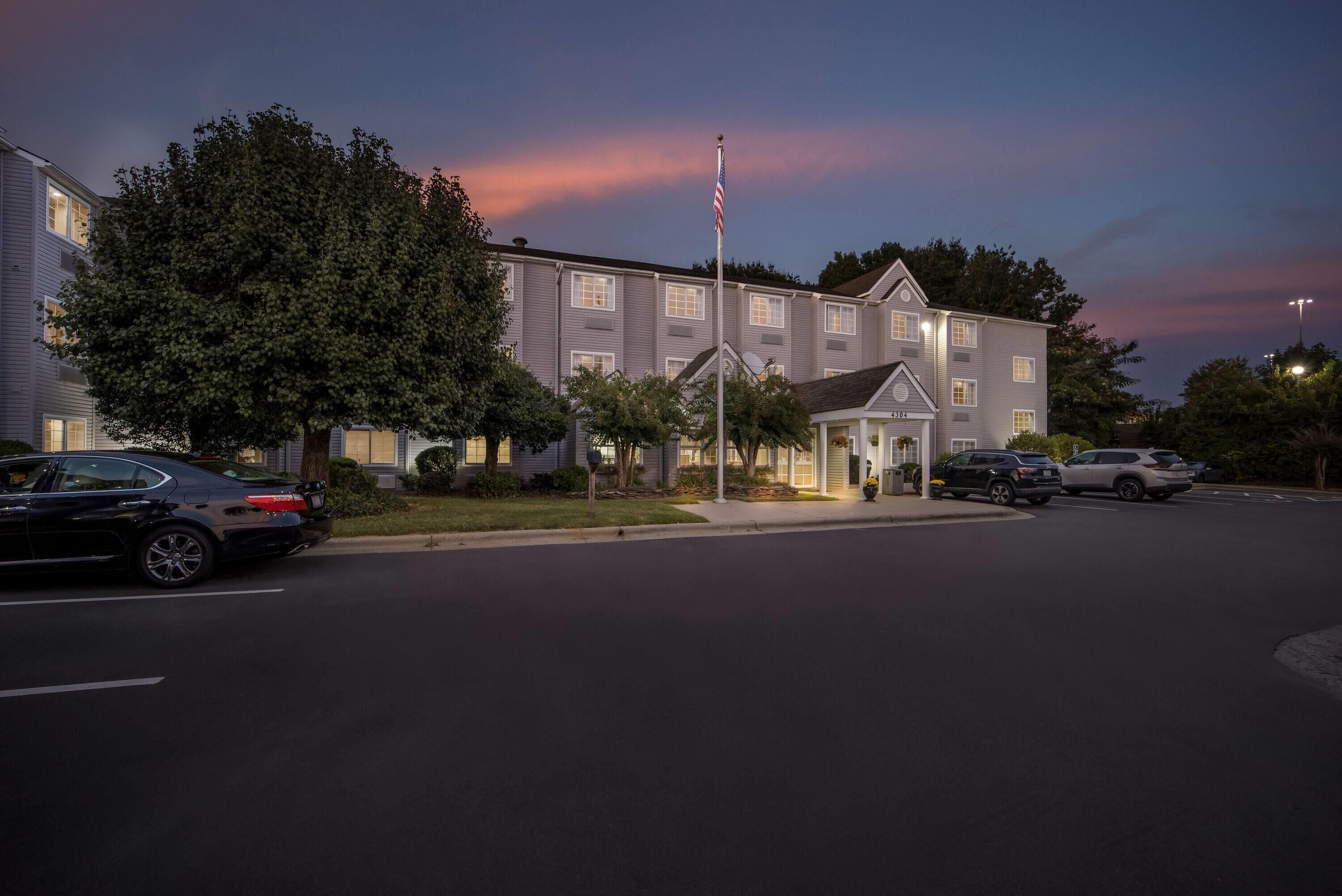 A multi-story hotel with a flagpole, parked cars, and a well-maintained lawn.
