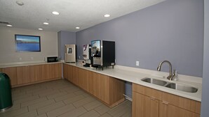 A modern kitchen with wooden cabinets, a stainless steel sink, a microwave, and a coffee machine. - Microtel Inn by Wyndham Greensboro (Greensboro)