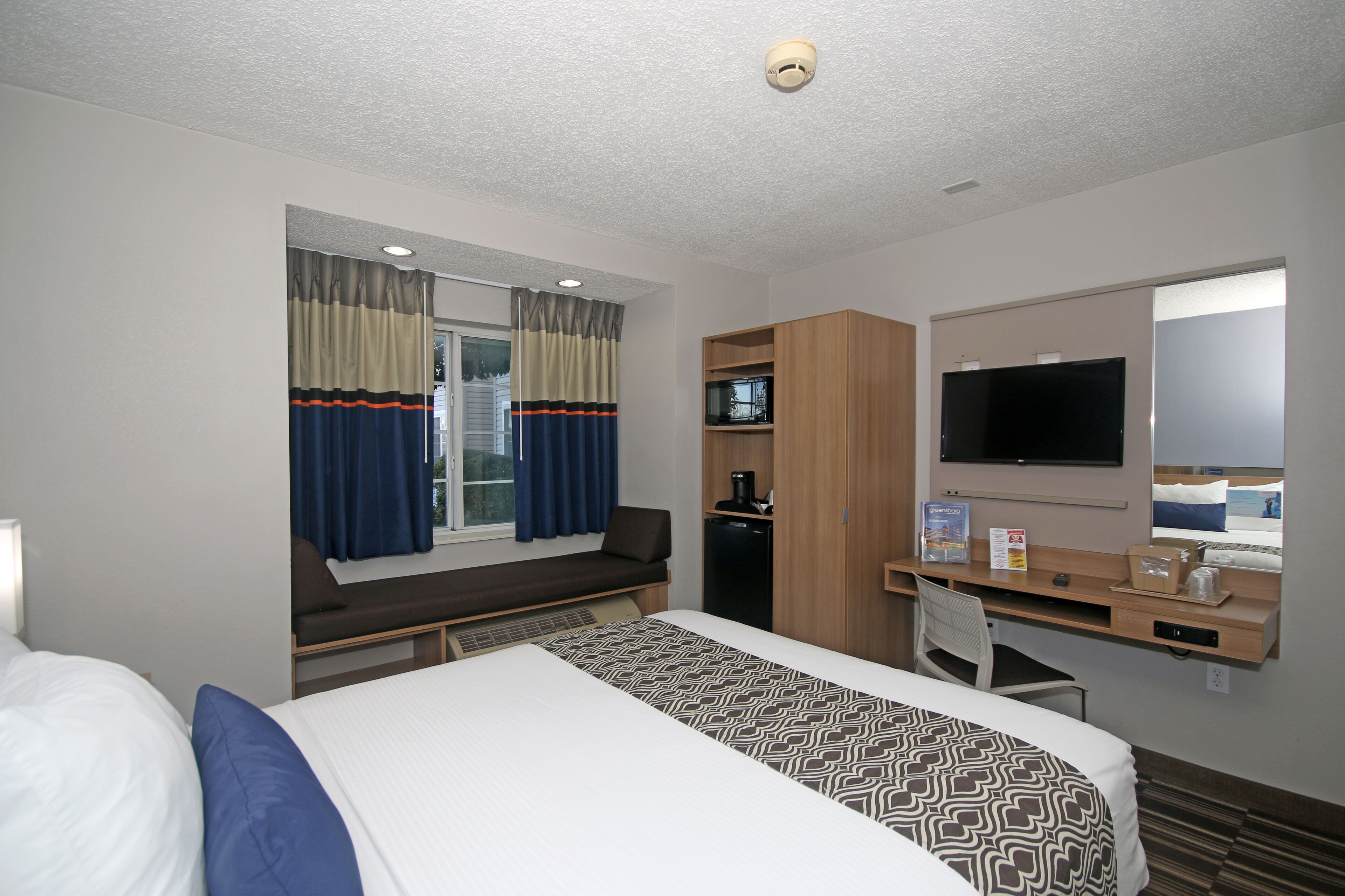 A hotel room with a bed, a desk with a computer, a TV, and a window with curtains.