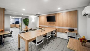 A modern conference room with a long wooden table, white chairs, a flat-screen TV mounted on the wall, and a potted plant. - Microtel Inn by Wyndham Greensboro (Greensboro)