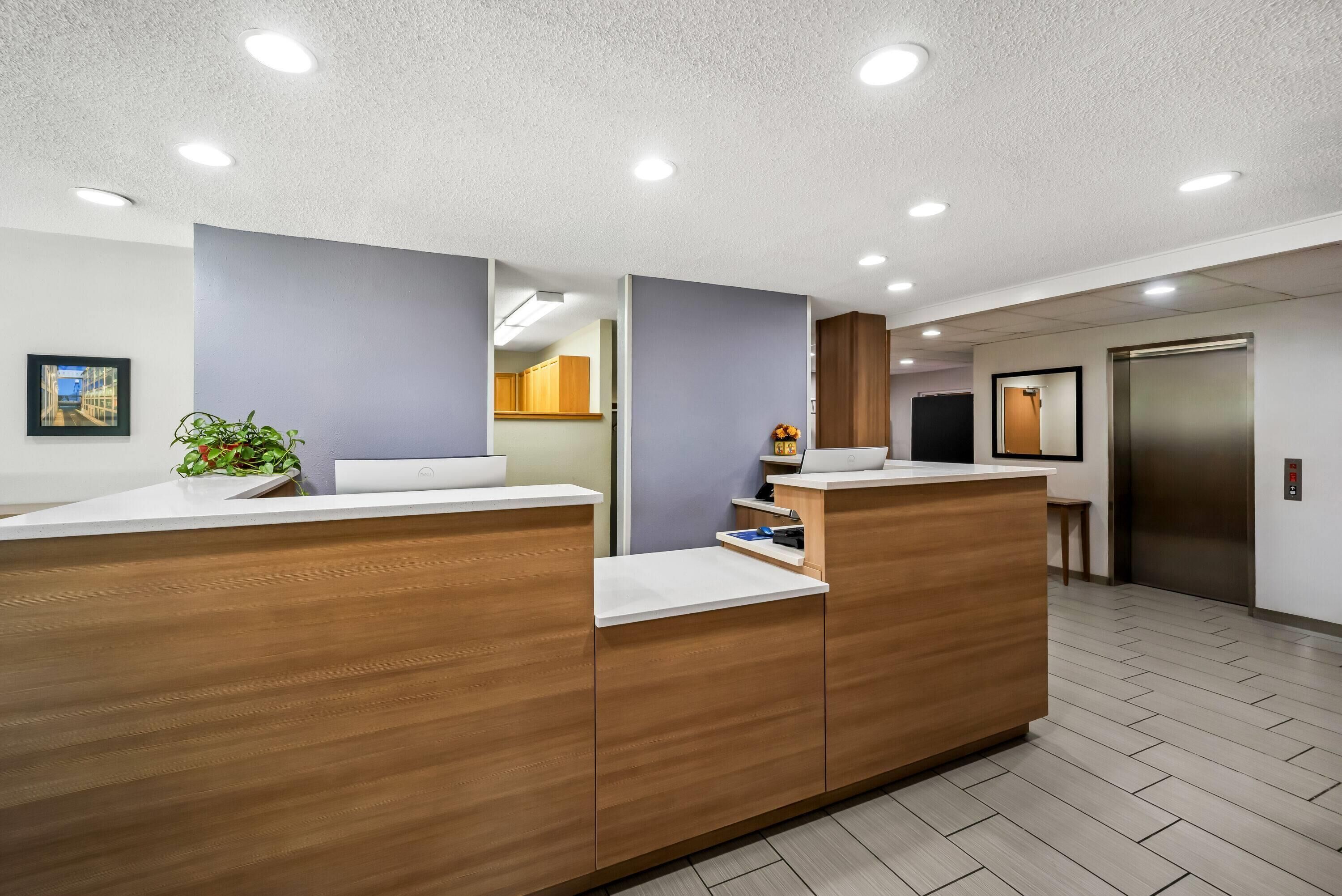 A reception area with wooden reception desks, a potted plant, and a framed picture on the wall.