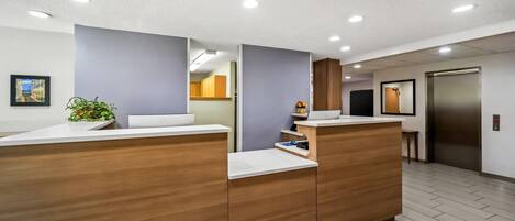 A reception area with wooden reception desks, a potted plant, and a framed picture on the wall.