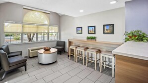 A modern waiting area with a round table, bar stools, and a large window offering a view of the street. - Microtel Inn by Wyndham Greensboro (Greensboro)