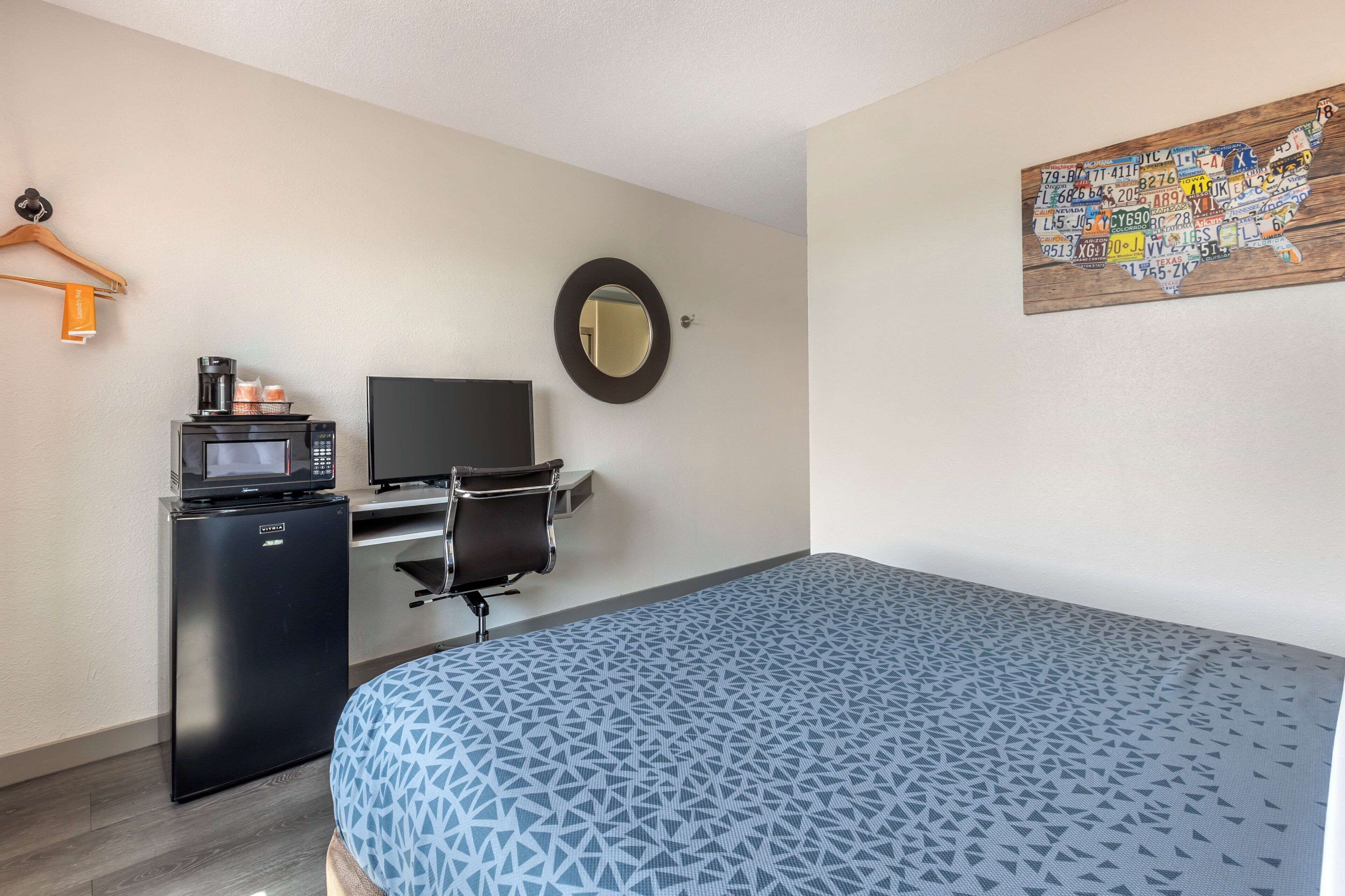 A hotel room with a bed, a desk with a computer, a microwave, and a small refrigerator.