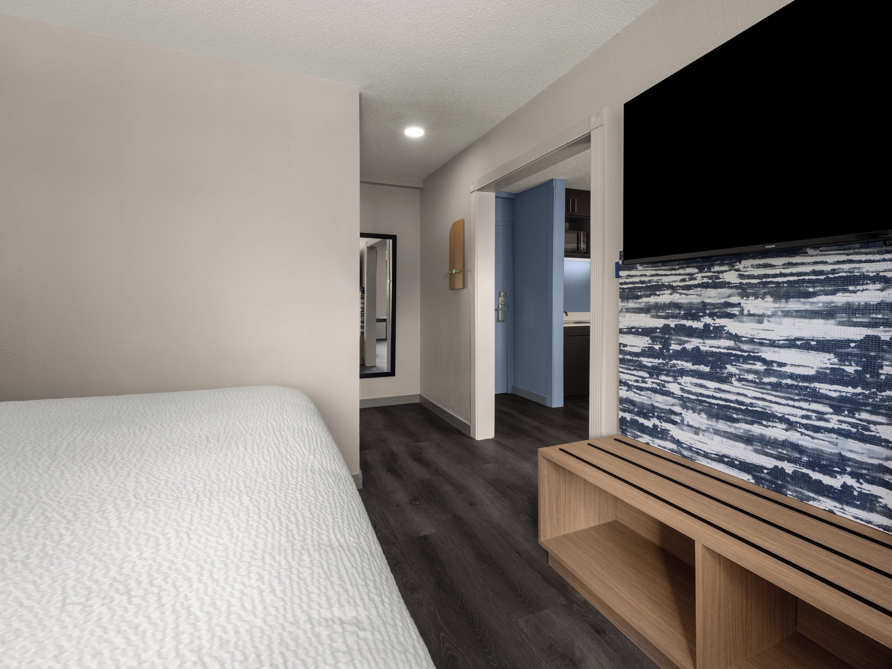 Une chambre d’hôtel comprenant un lit, une banquette, un téléviseur fixé au mur et une porte donnant accès à une salle de bain.