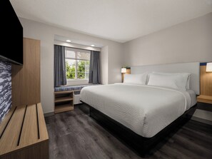Ein Hotelzimmer mit einem großen Bett, einer Sitzbank inklusive Stauraum, einem Fernseher und einem Fenster mit Vorhängen.