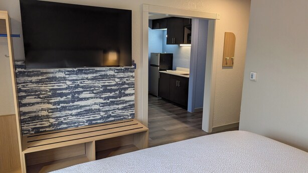 Een kleine kamer met een bed, een bureau, een televisie en een kitchenette.