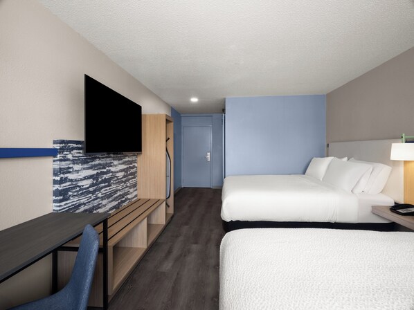 Una habitación de hotel con una cama, un escritorio, una silla, un televisor y una puerta.