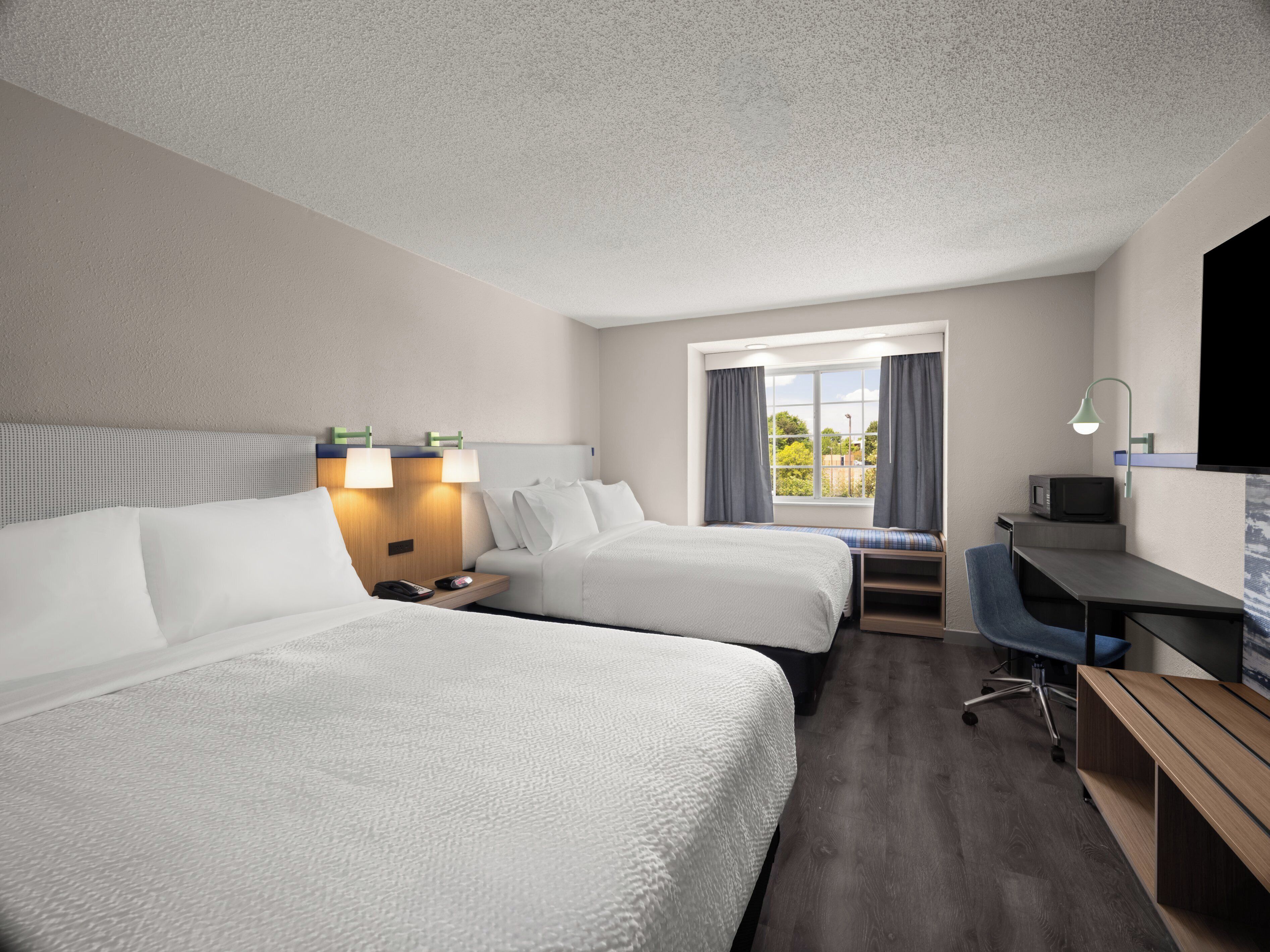 A hotel room with two beds, a desk, a chair, a TV, and a window with curtains.