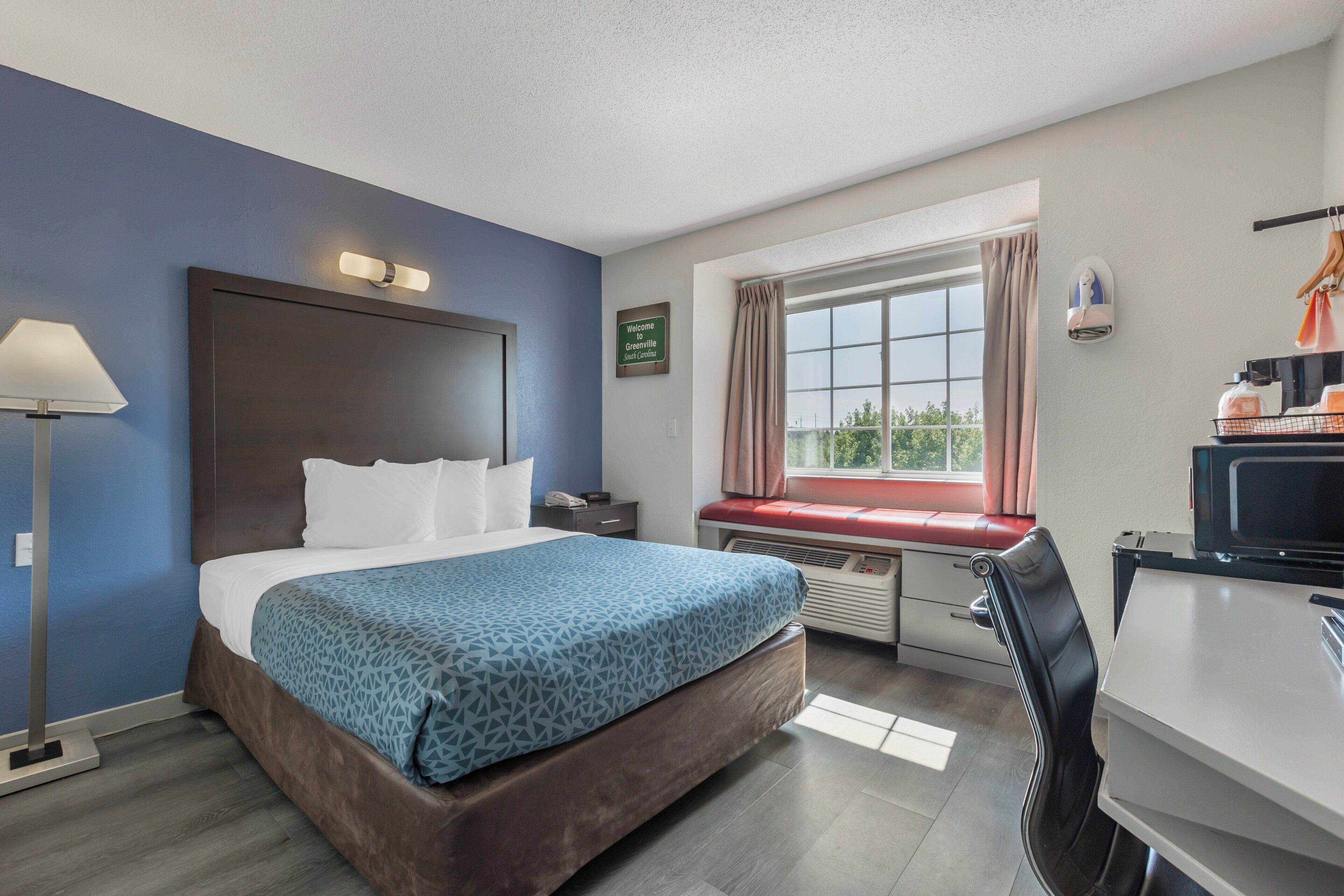 Habitación de hotel con cama, mesita de noche, lámpara, ventana con cortinas y escritorio con silla.