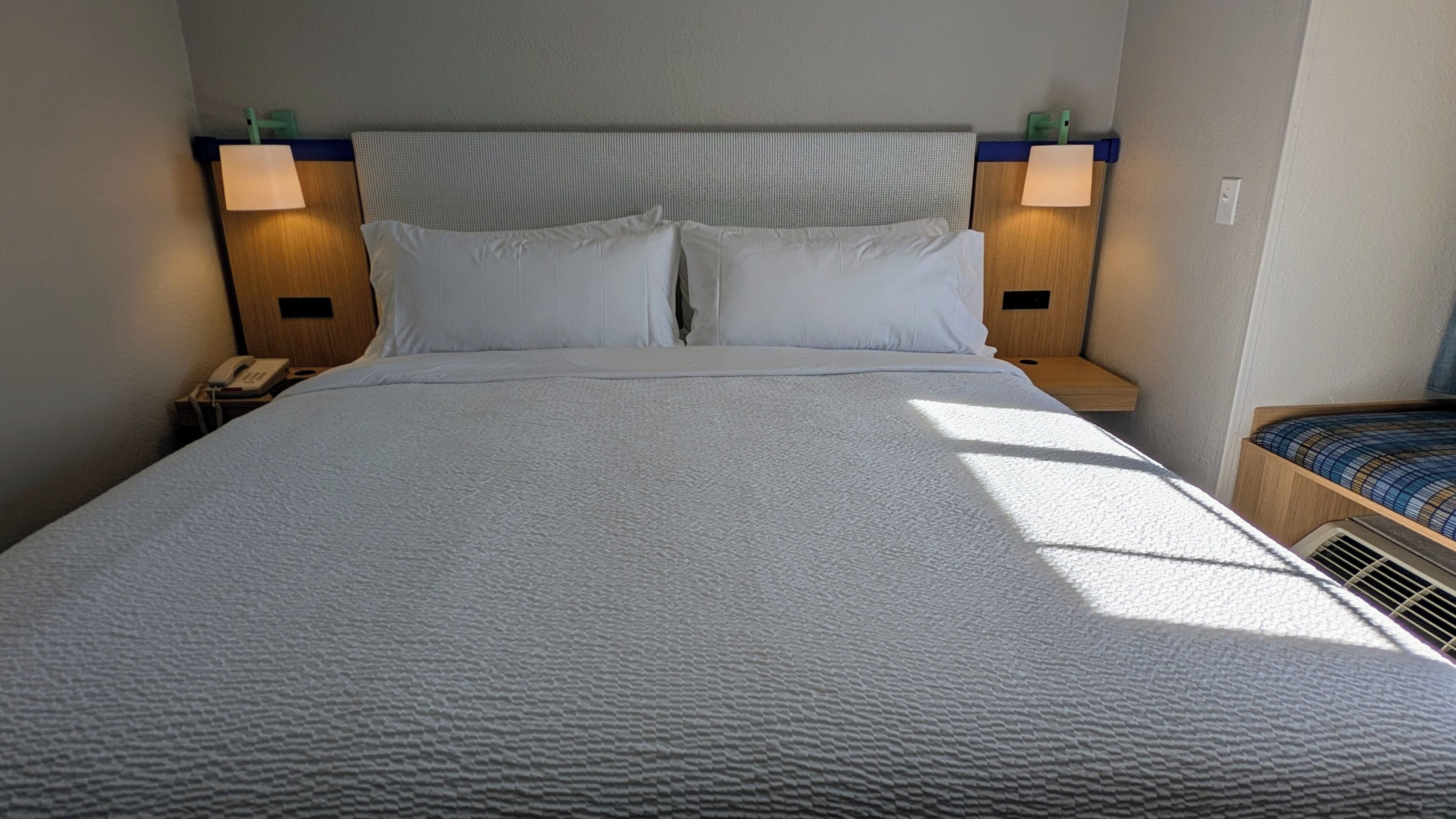 Un lit avec une couette blanche à motifs, deux oreillers et une tête de lit agrémentée de deux lampes de chevet.