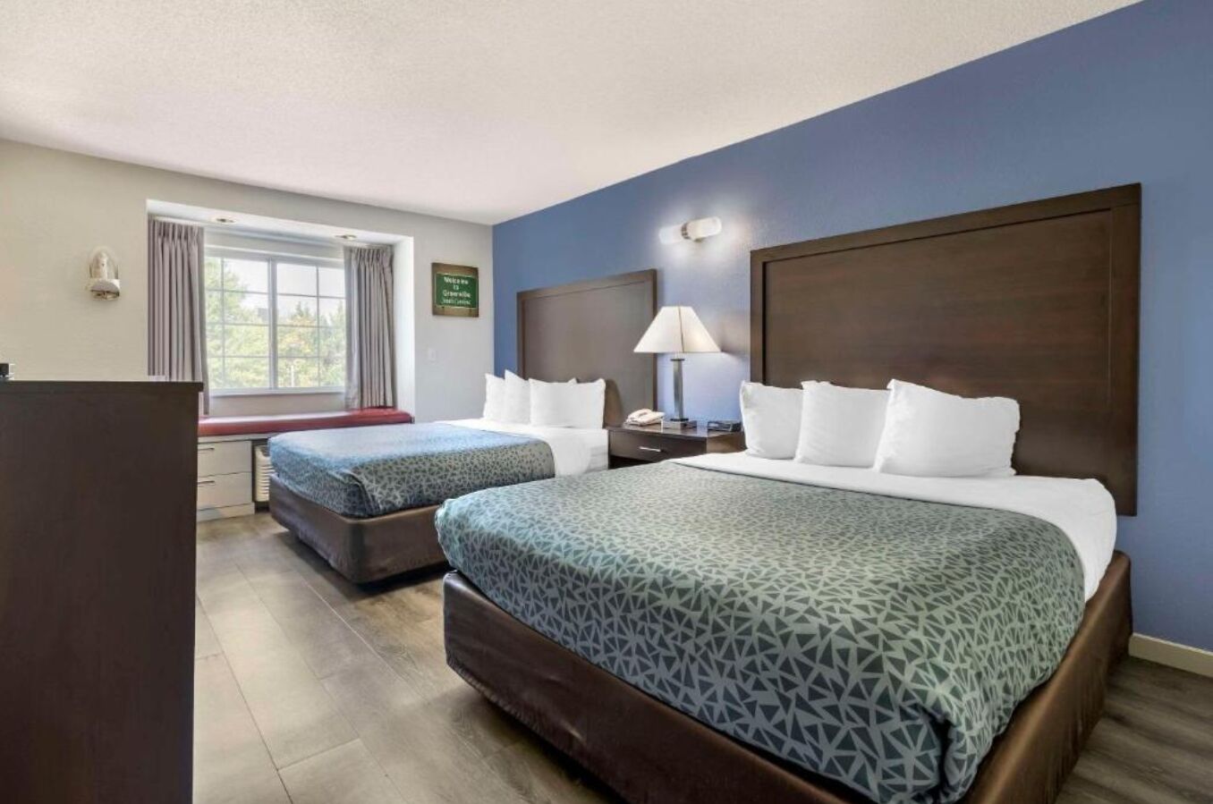 Habitación de hotel con dos camas, un escritorio, una lámpara y una ventana con cortinas.