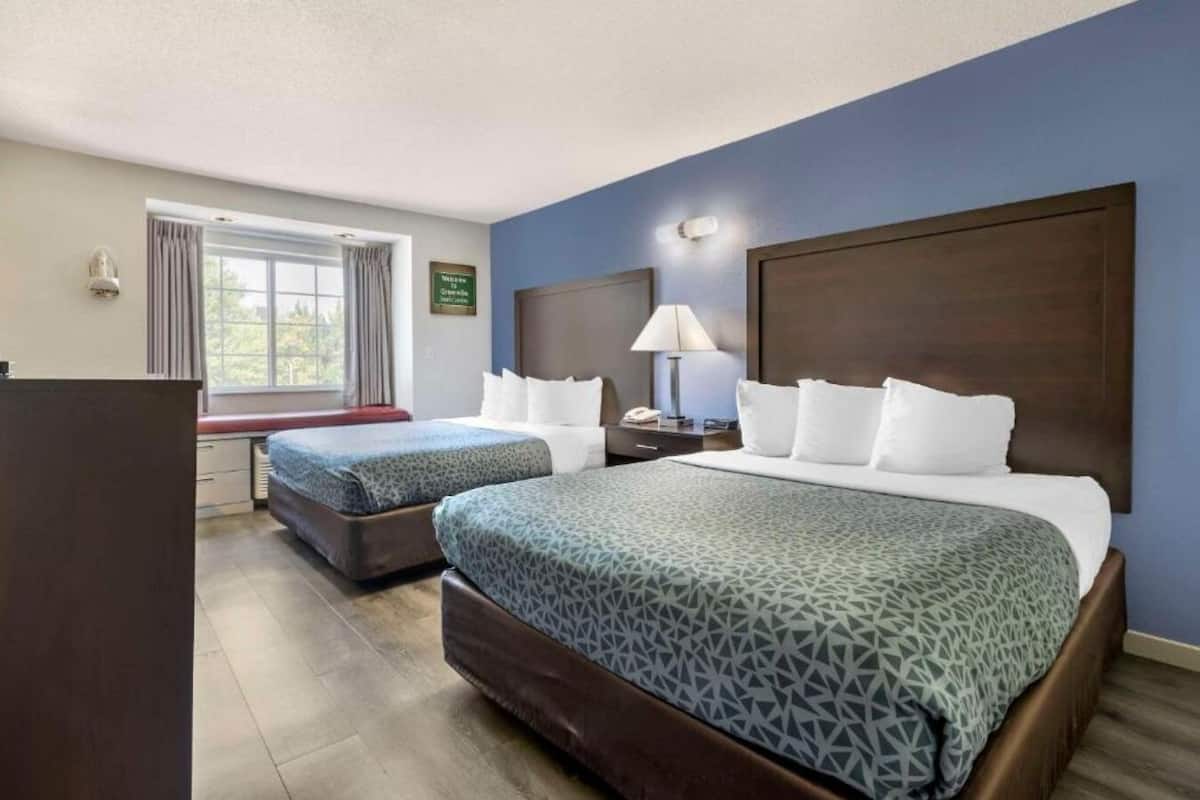 Habitación de hotel con dos camas, un escritorio, una lámpara y una ventana con cortinas.
