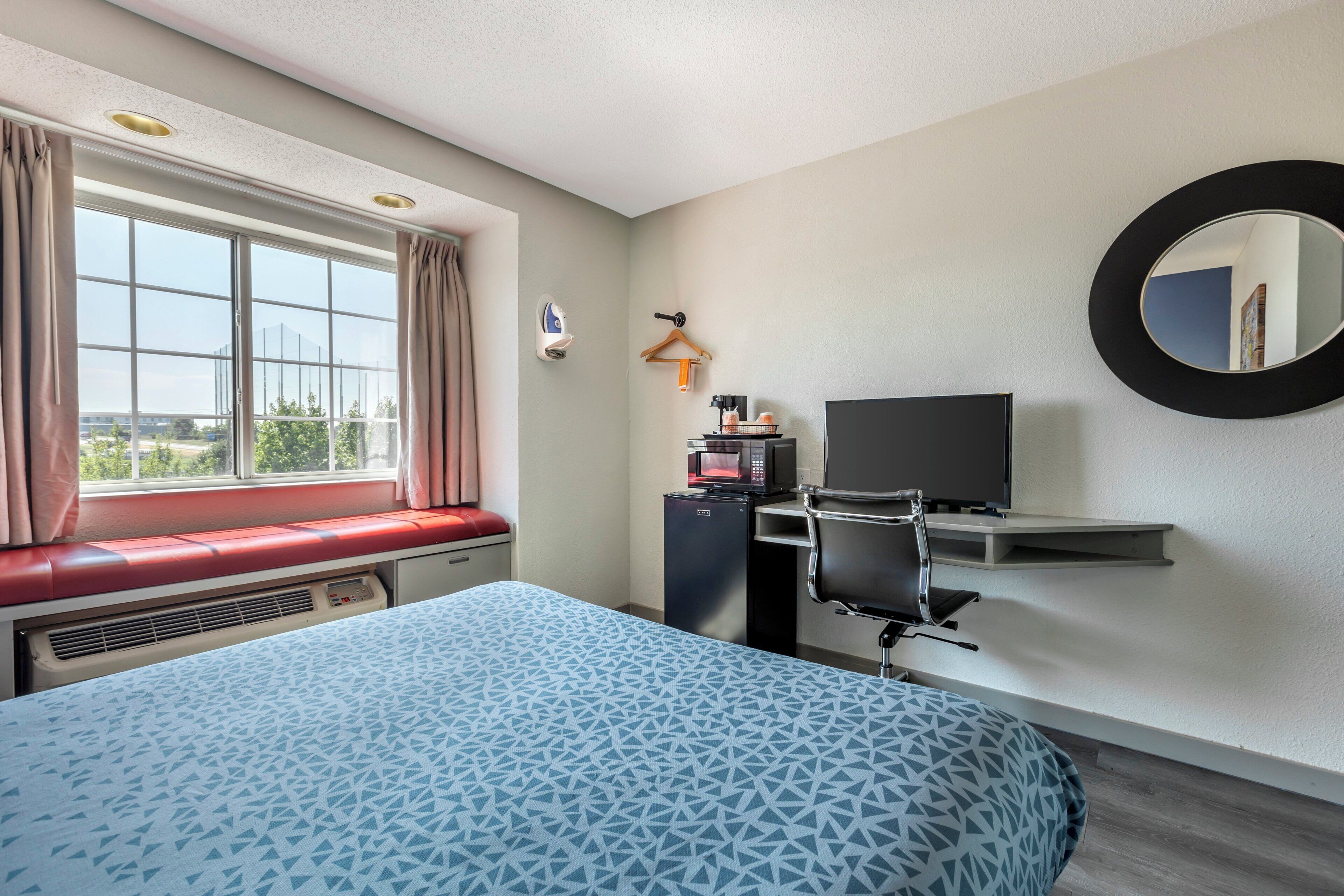 A hotel room with a bed, a desk, a chair, a television, and a window with curtains.