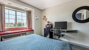 A hotel room with a bed, a desk, a chair, a television, and a window with curtains.