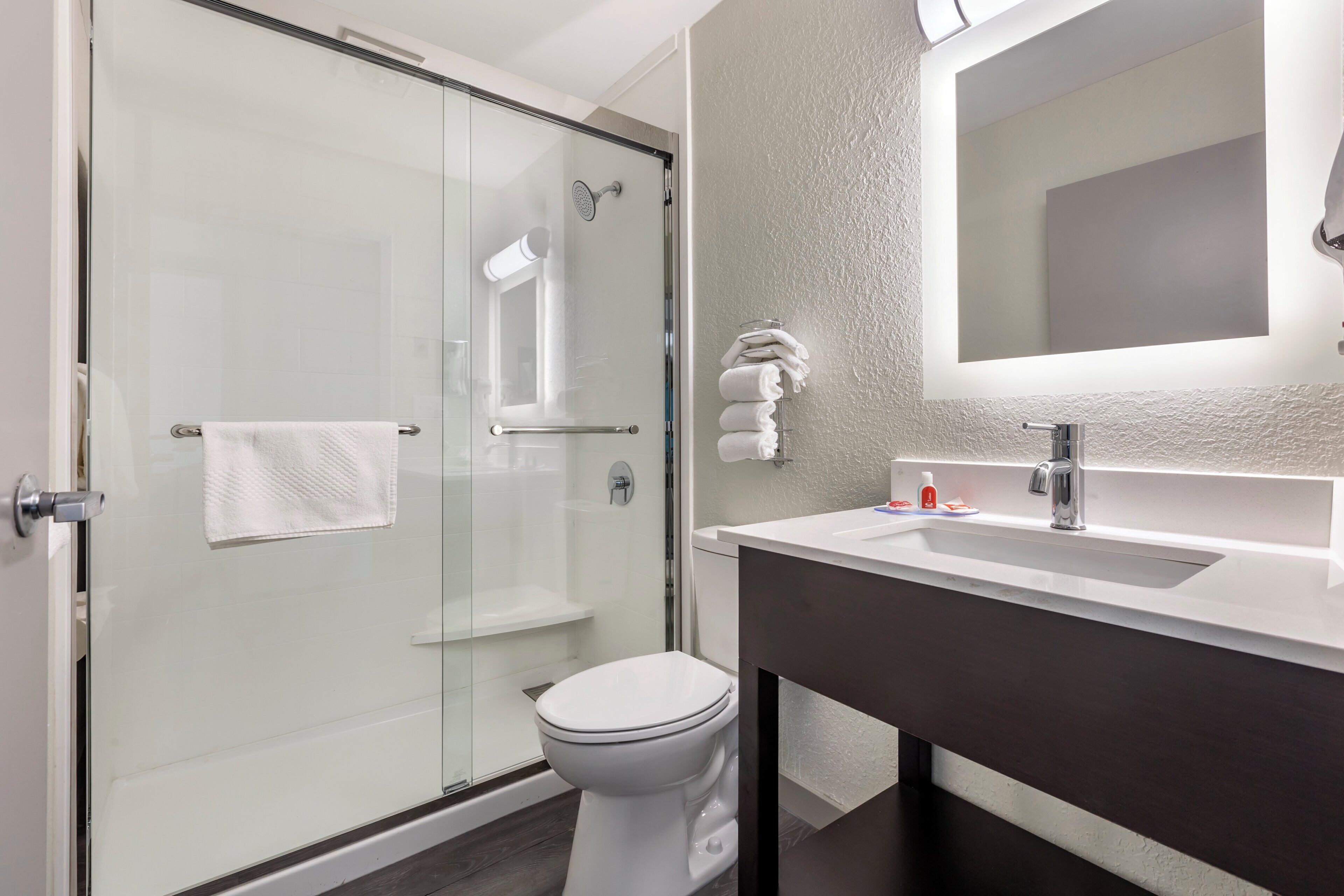 Un baño moderno con cabina de ducha de vidrio, inodoro blanco y tocador con espejo.