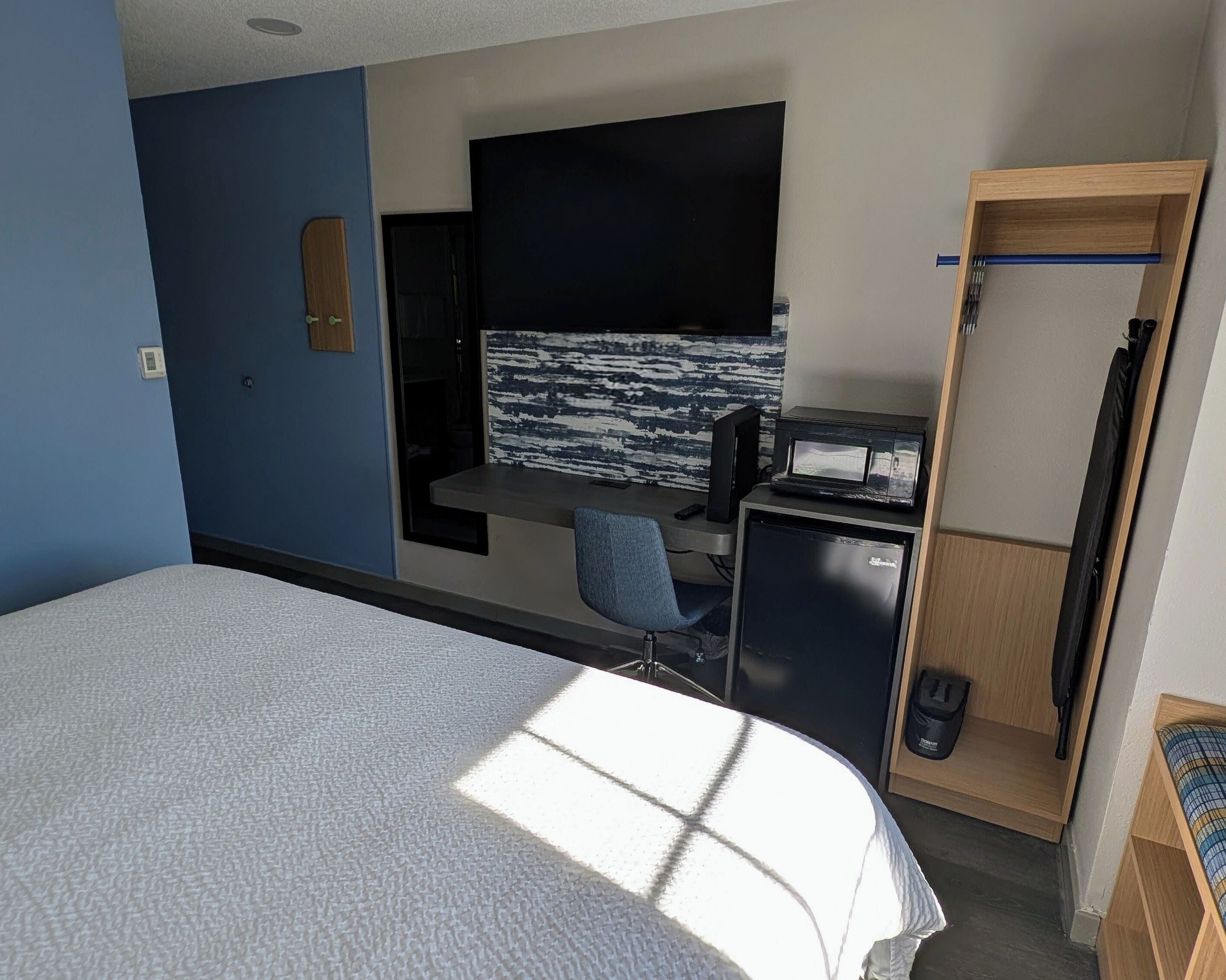 Habitación de hotel con cama, escritorio con computadora, televisor y una kitchenette pequeña.