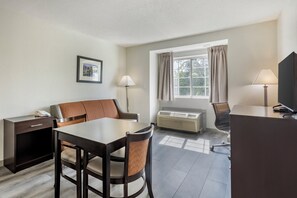 A hotel room with a dining table, two chairs, a desk, a telephone, a lamp, and a window with curtains. - Garner Hotel Greenville East by IHG (Greenville)