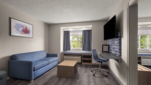 Ein modernes Zimmer mit einer Couch, einem Schreibtisch, einem Stuhl, einem Flachbildfernseher und einem fenster mit Vorhängen.