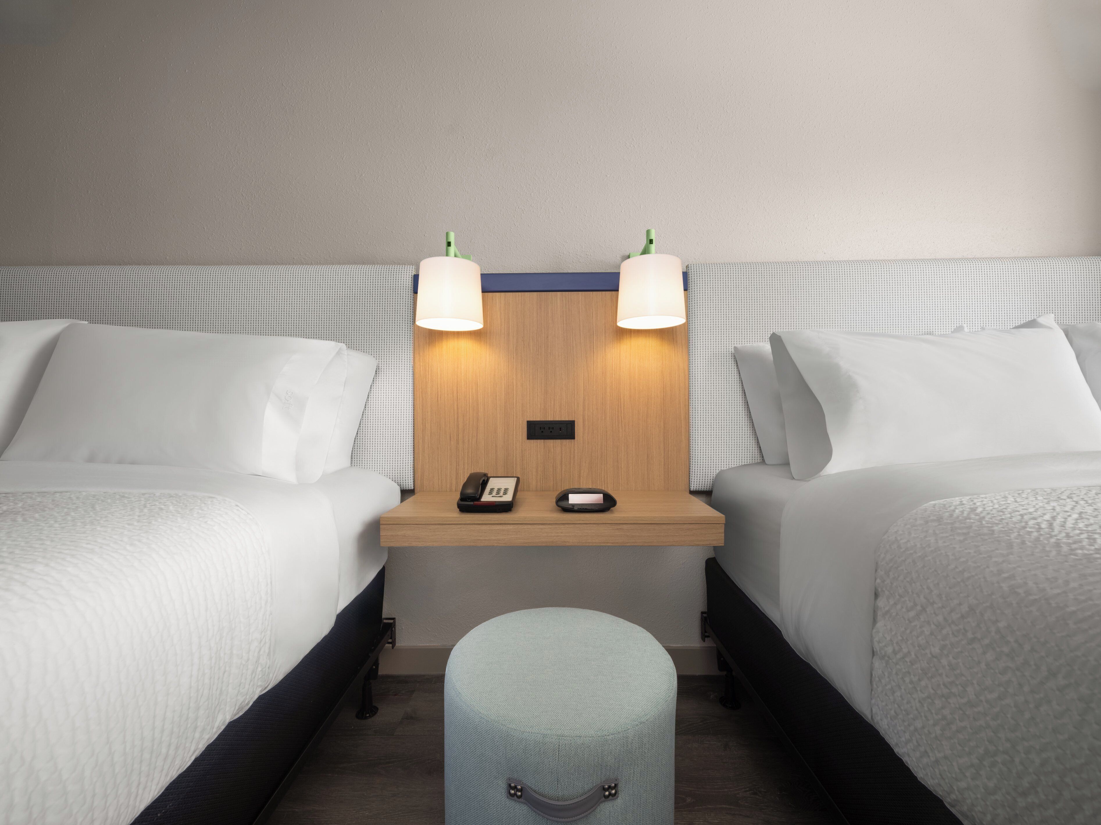 Ein Hotelzimmer mit zwei Betten, einem Nachttisch mit Lampe, einem Telefon und einem kleinen Hocker.