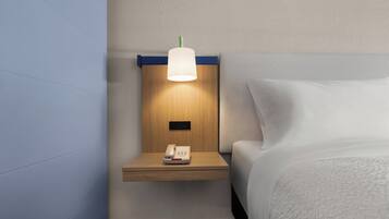 Habitación de hotel con mesita de noche de madera, lámpara, teléfono y cama con ropa blanca.