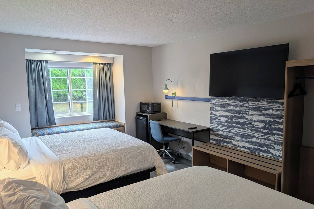 Una habitación de hotel con dos camas, un escritorio con ordenador, televisión y ventana con cortinas.