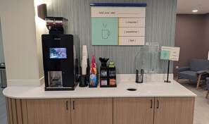 Espai preparació cafè amb cafetera, dosificadors d'ingredients i cartell per afegir elements personals.