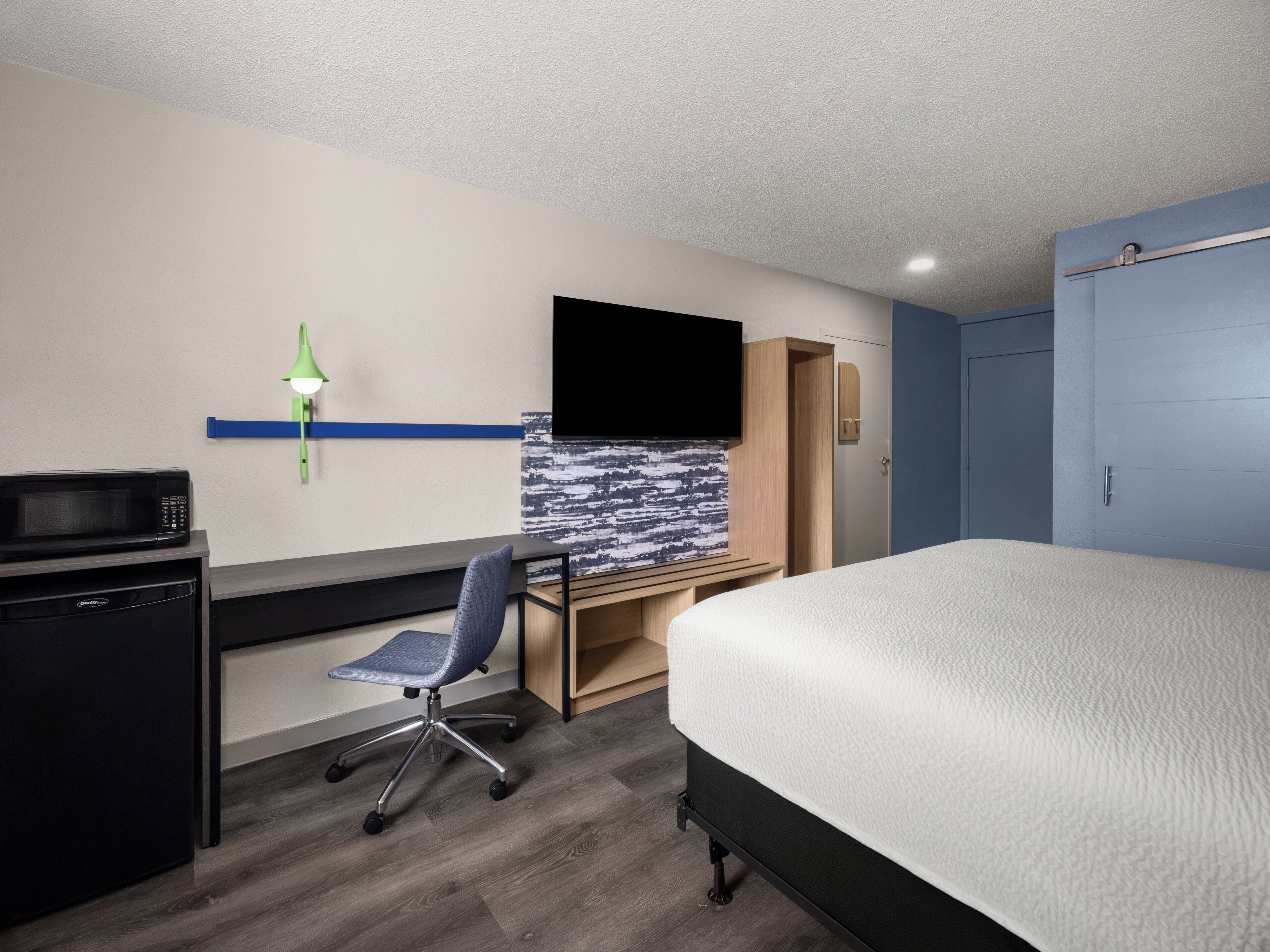 A hotel room with a bed, desk, chair, microwave, and TV.