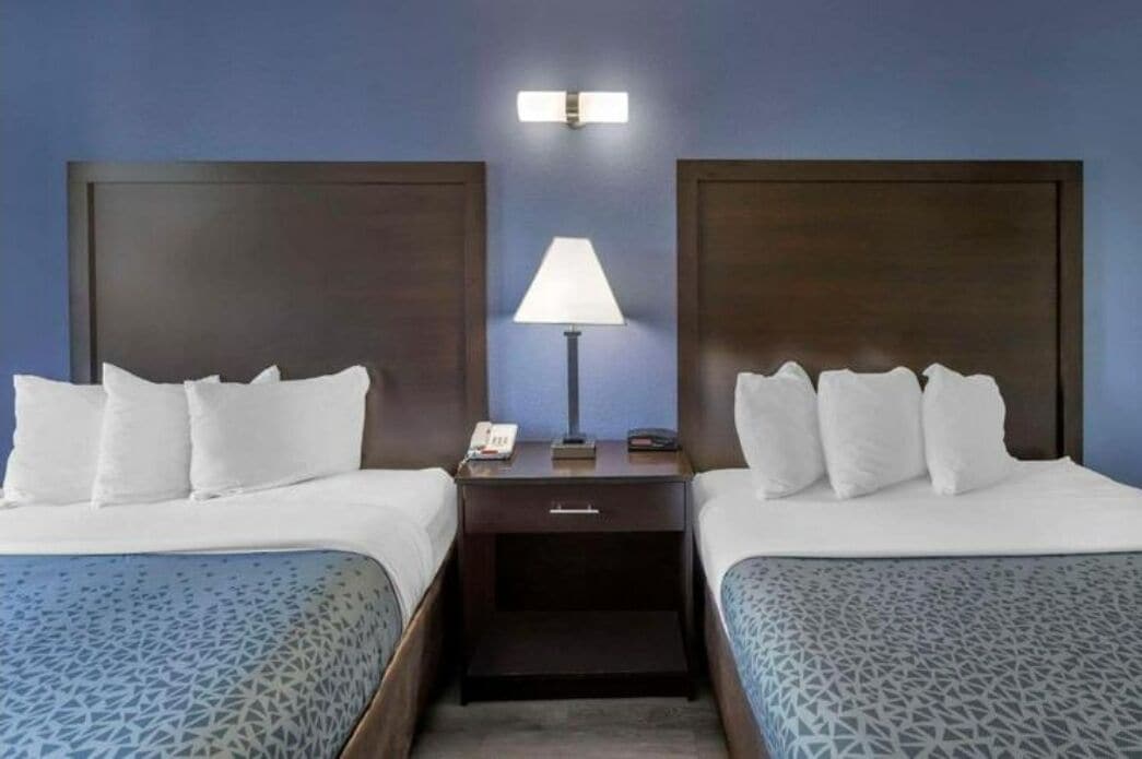 Una habitación de hotel con dos camas, una mesita de noche con lámpara y un aplique de pared.