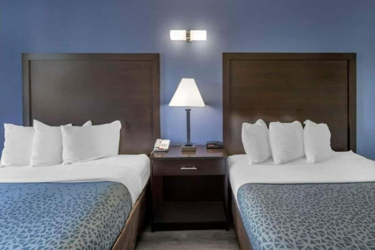 Una habitación de hotel con dos camas, una mesita de noche con lámpara y un aplique de pared.
