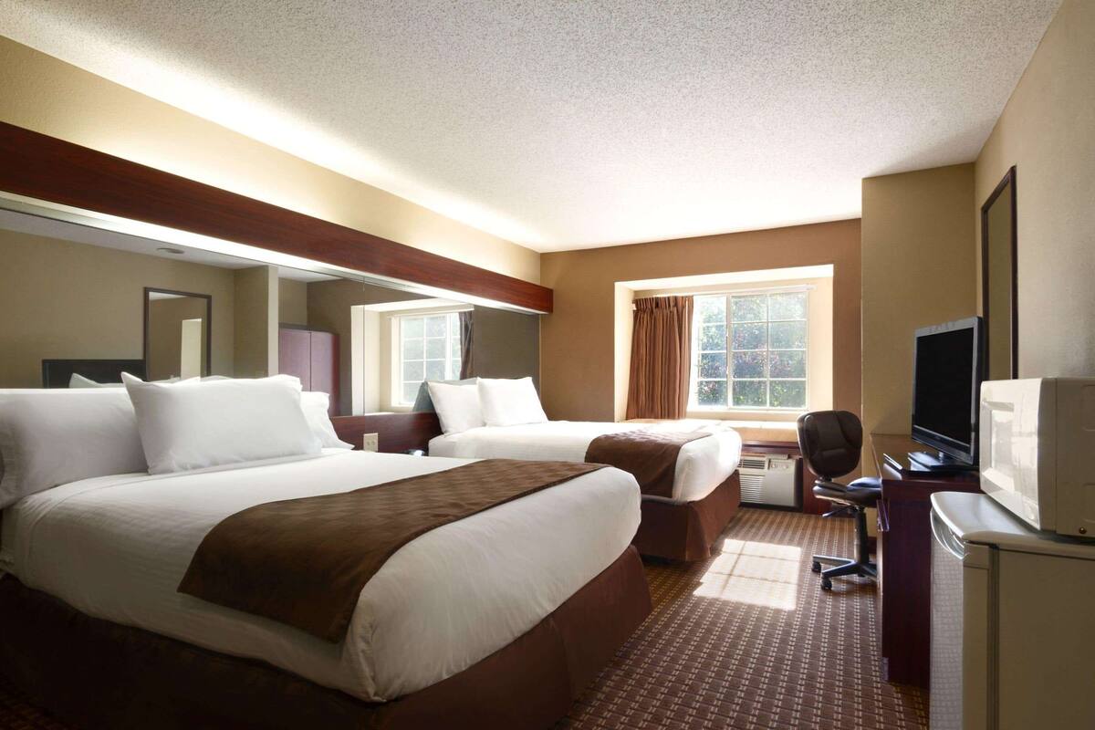 Una habitación de hotel con dos camas, un escritorio, un televisor y una ventana con cortinas.