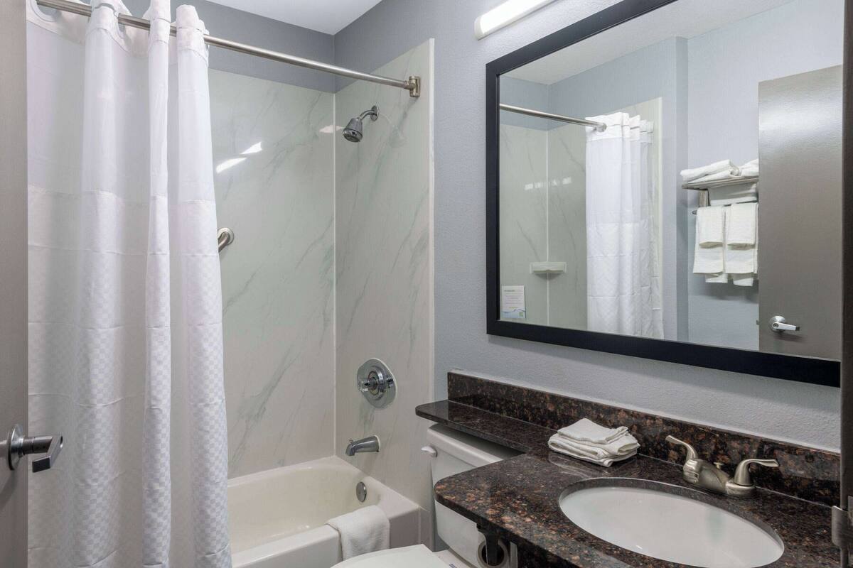 Un baño con ducha, bañera, lavamanos y espejo.