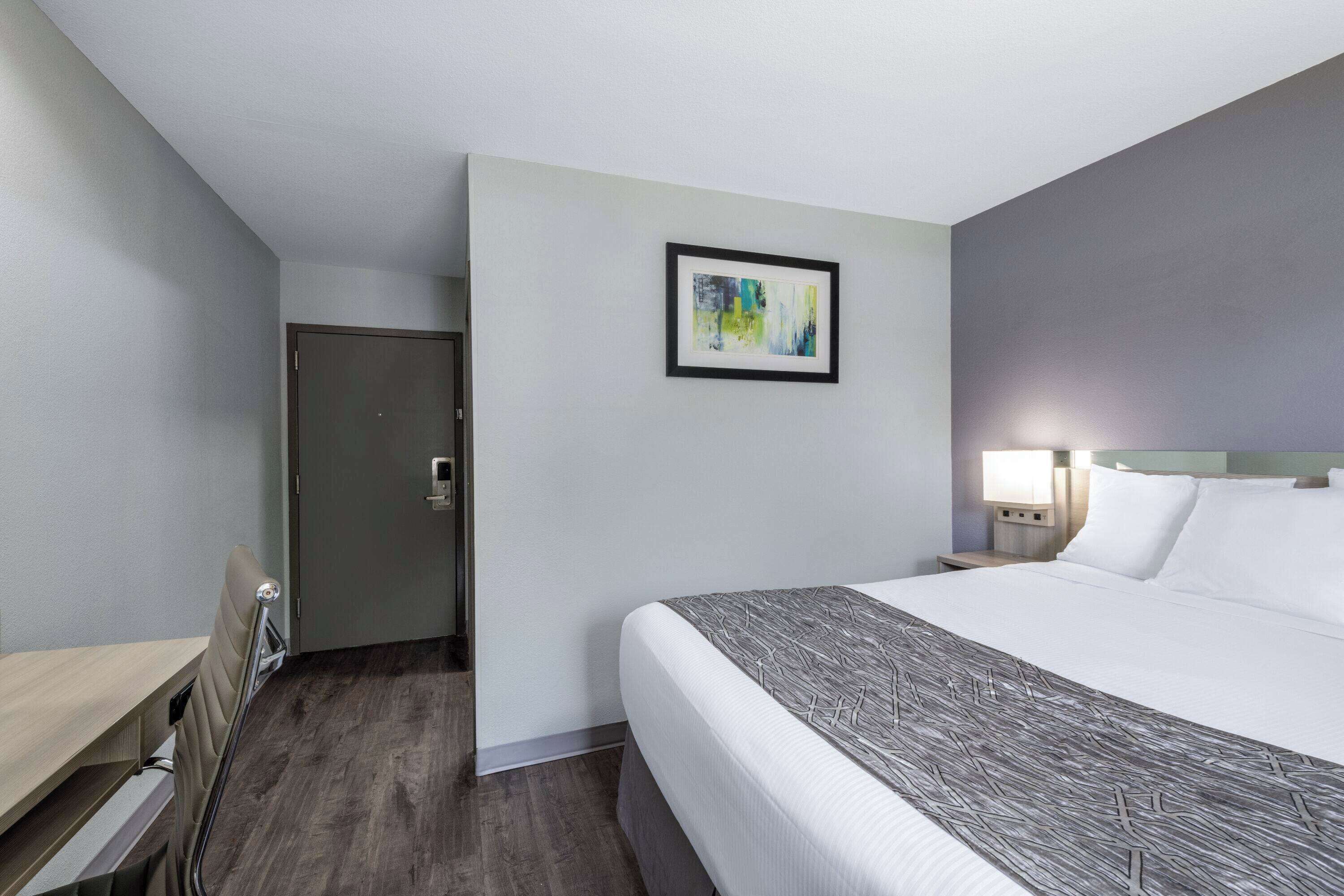 Una habitación de hotel con cama, mesita de noche, lámpara y puerta.