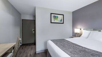 A hotel room with a bed, bedside table, lamp, and a door.