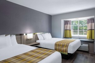 Habitación de hotel con dos camas, una ventana con cortinas, una mesita de noche y una lámpara de pared.