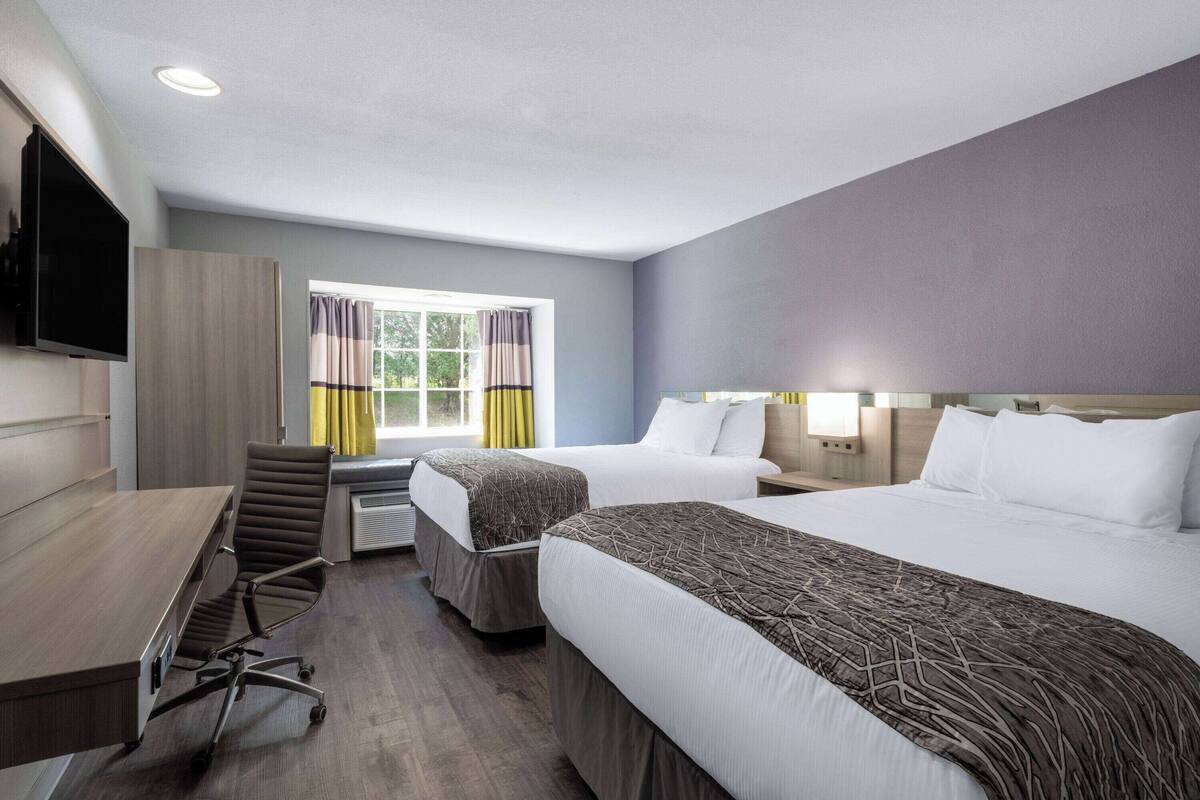 Habitación de hotel con dos camas, un escritorio, una silla, un televisor y un ventanal con cortinas.