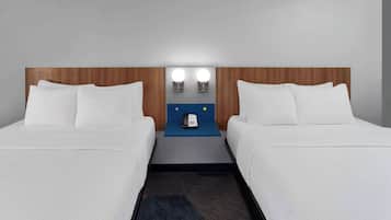 A hotel room with two beds, a wooden headboard, a blue nightstand with a phone, and two wall-mounted lights.