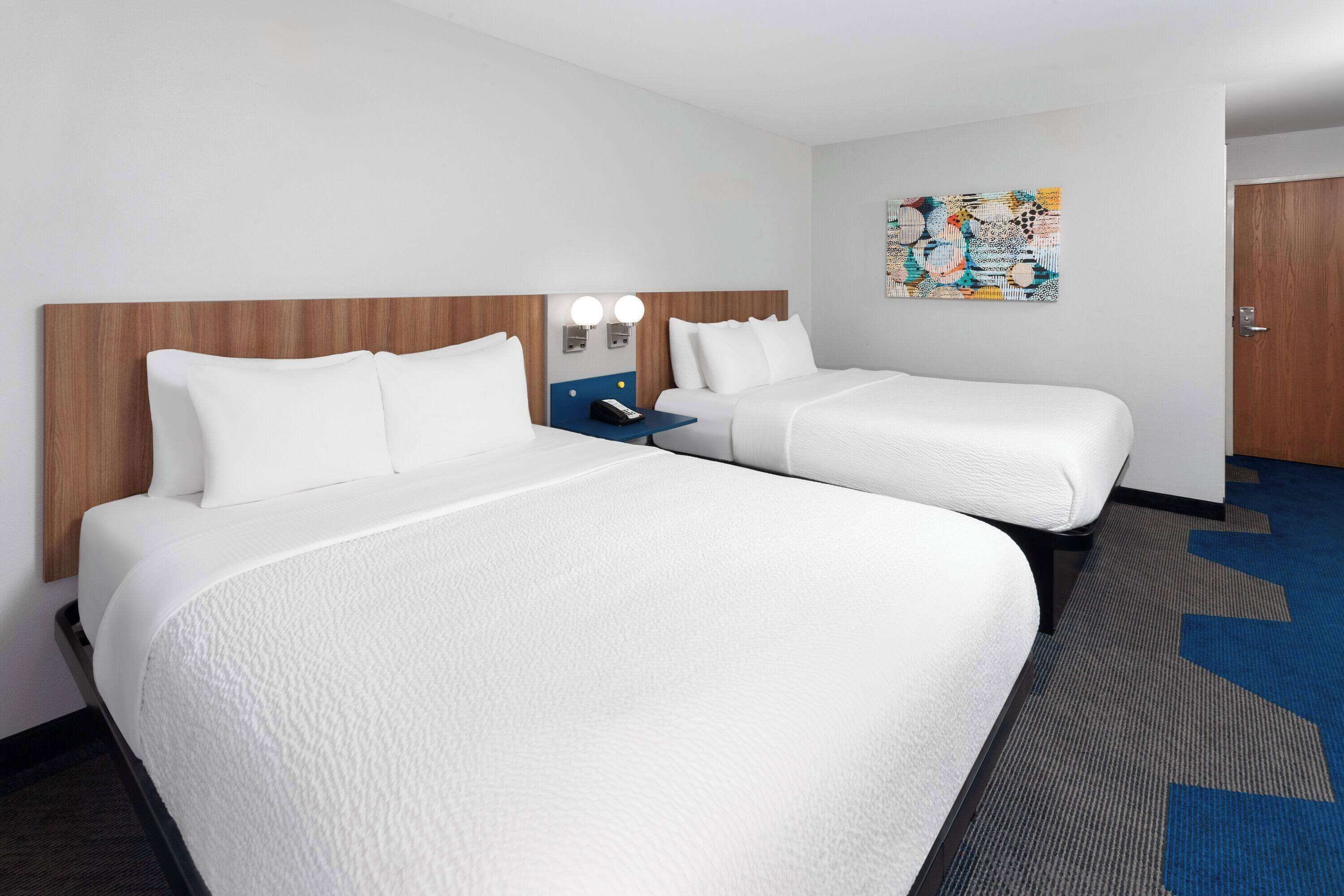 A hotel room with two beds, a small desk, and a wall-mounted artwork.