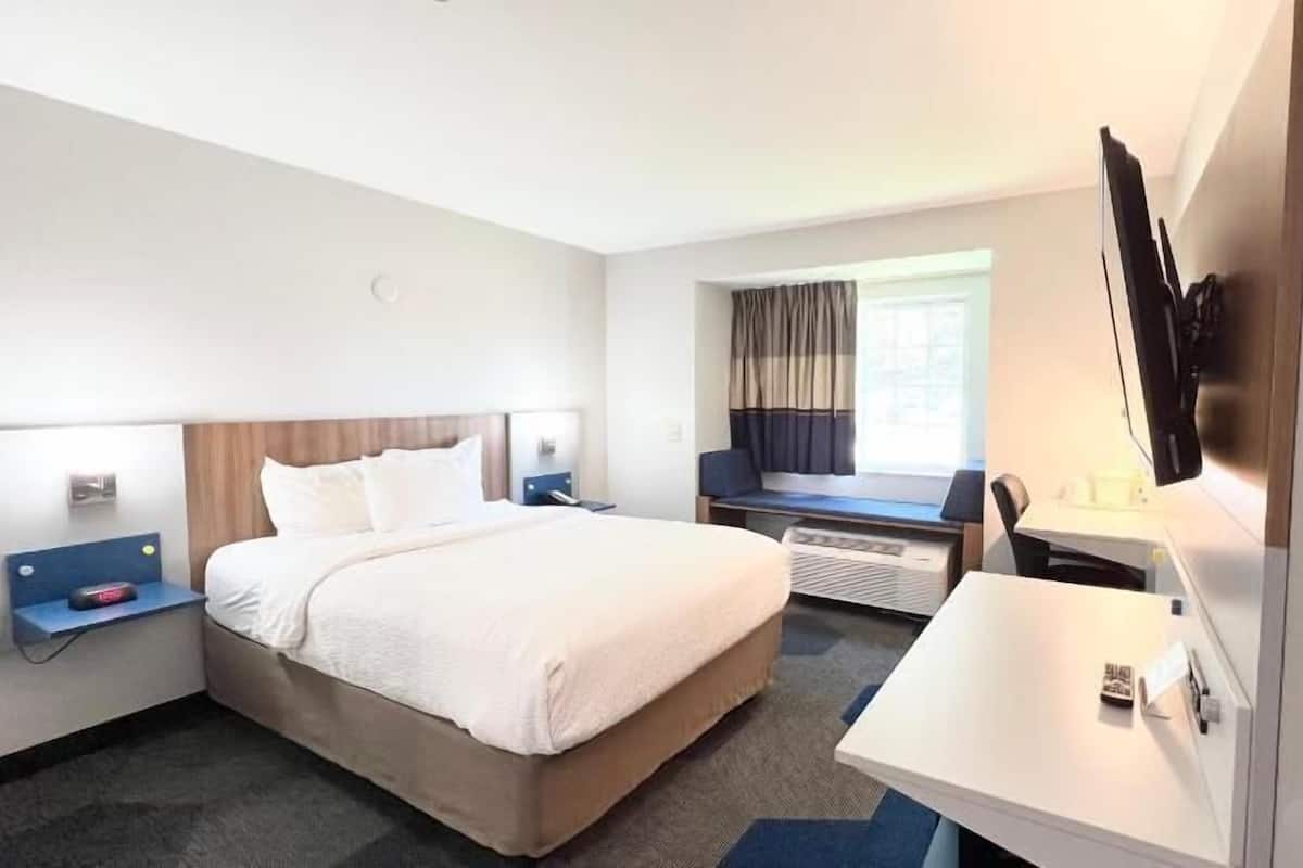 Una habitación de hotel con cama, mesitas de noche, escritorio, televisor y ventana con cortinas.