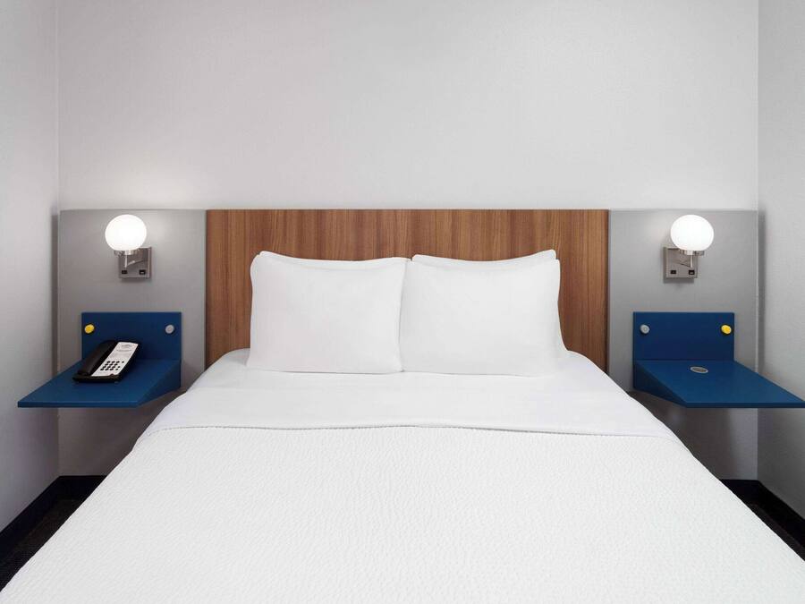Quarto de hotel com cama, duas mesas de cabeceira e cabeceira de madeira.