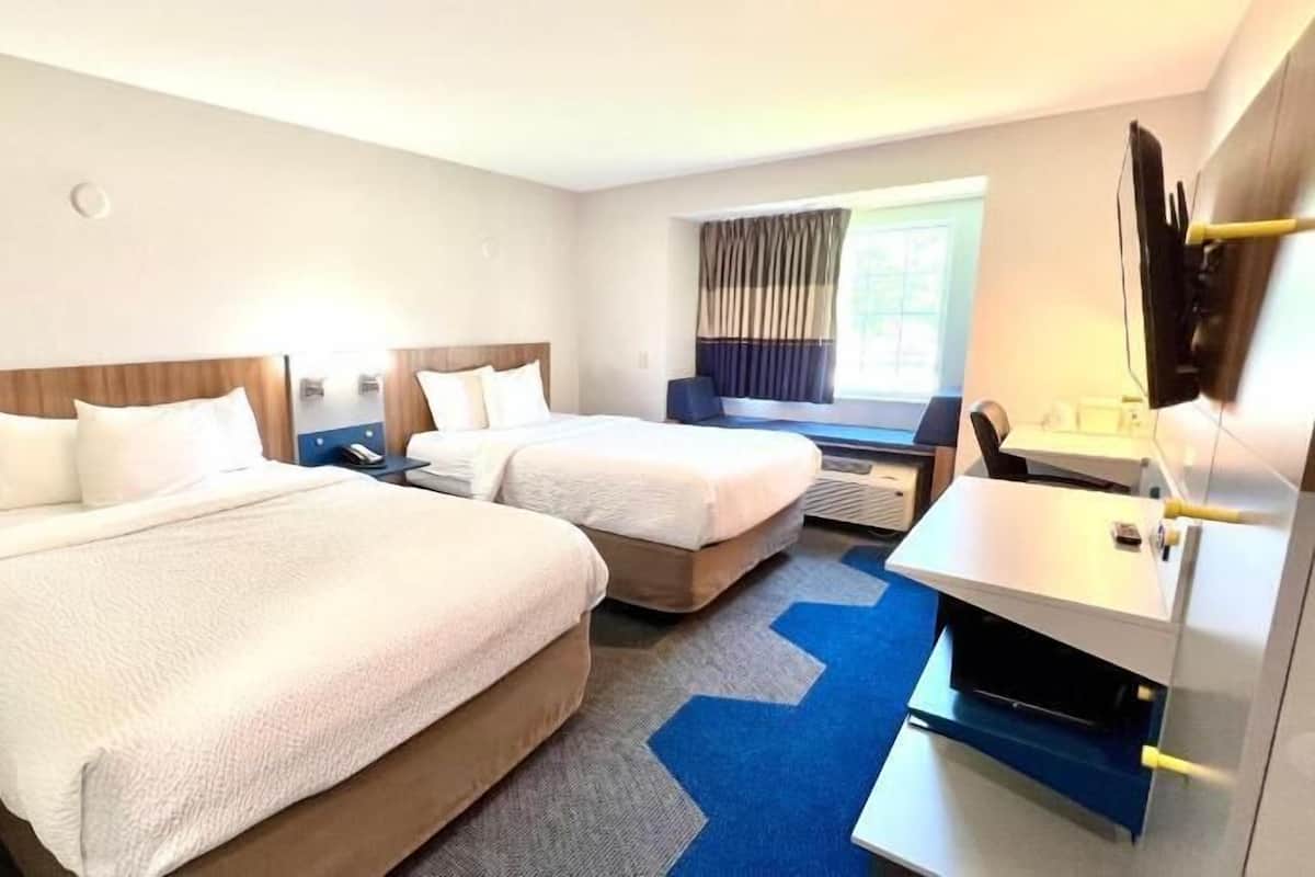 Habitación de hotel con dos camas, un escritorio, una silla, un televisor y una ventana con cortinas.