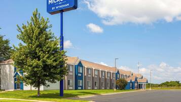 Un hotel Microtel Inn by Wyndham con un cielo azul despejado, un estacionamiento y un árbol en primer plano.