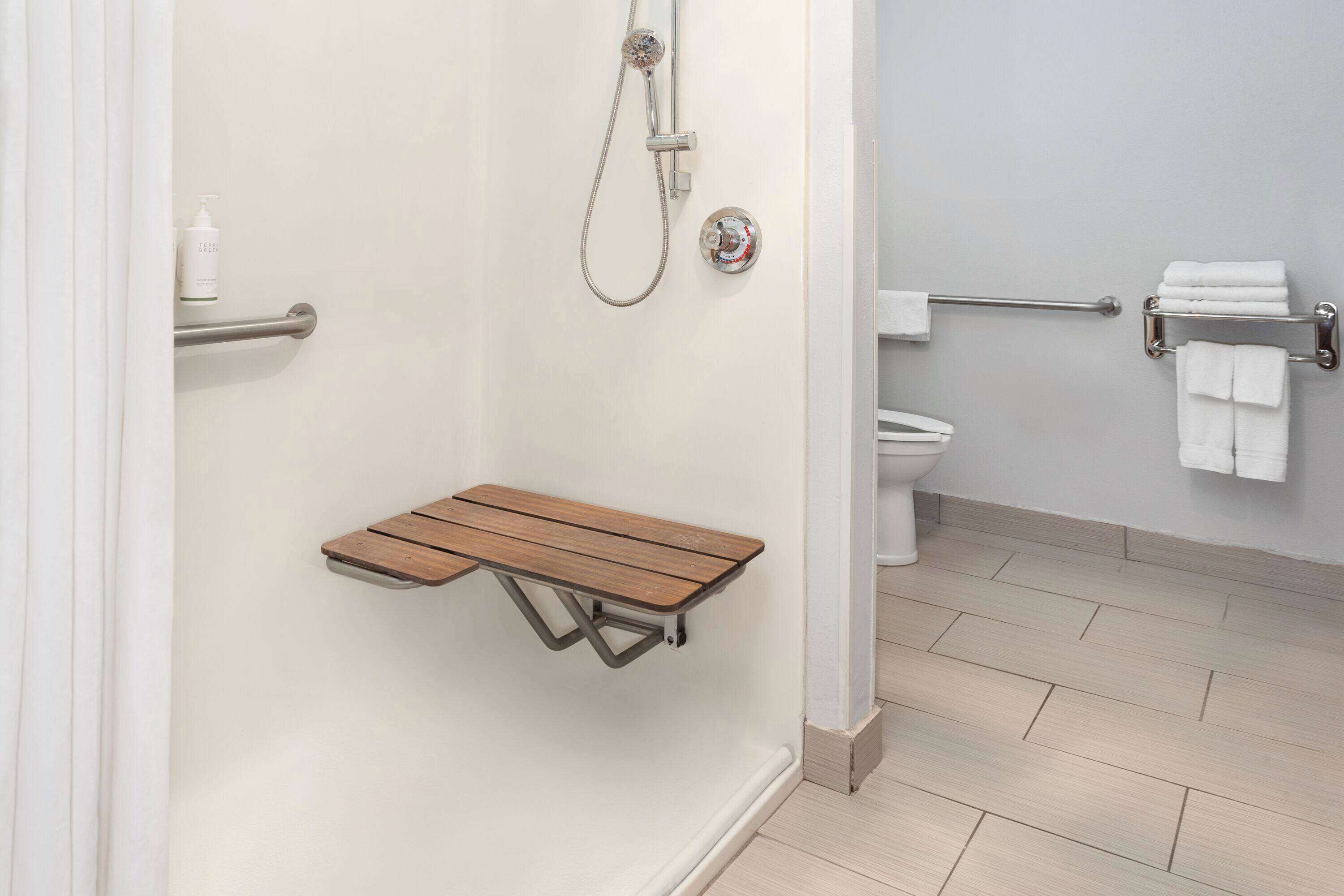 A bathroom with a shower, toilet, and a wooden bench.