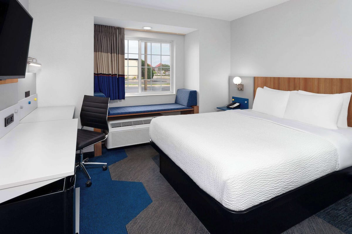 Habitación de hotel con cama, escritorio, silla y ventana con cortinas.