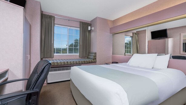 A hotel room with a large bed, a desk, a chair, a television, and a window with curtains. - Microtel Inn by Wyndham Onalaska/La Crosse (Onalaska)